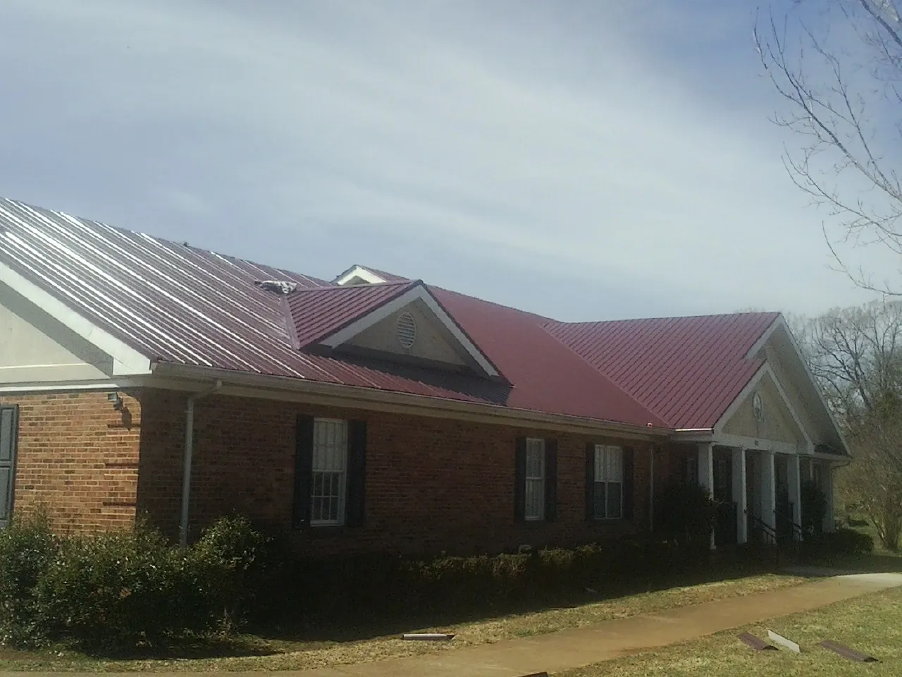 Red metal roof with gabled entries on a long brick building, from a Hail Damage Roof Repair job in Elkins Park