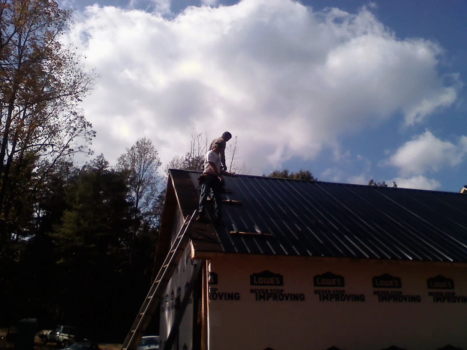 Roofer fastening dark metal panels high against a cloudy sky, from a Roof Inspection job in Elkins Park