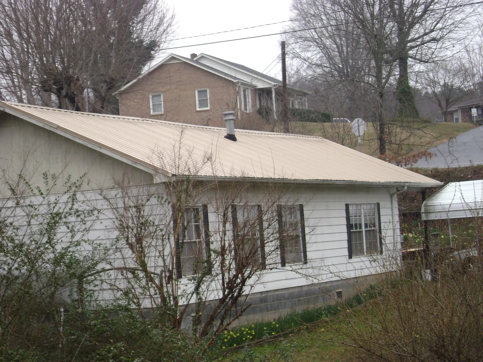 Tan metal roof on a white sided house set into a hillside — Commercial Roofing by Roofing Brothers in Elkins Park