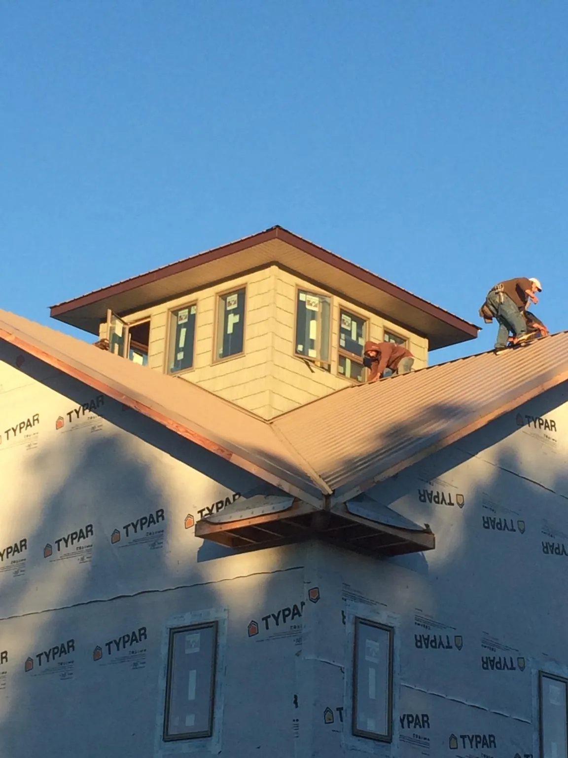 Roofers working around a rooftop cupola on a new metal roof at sunset in Elkins Park